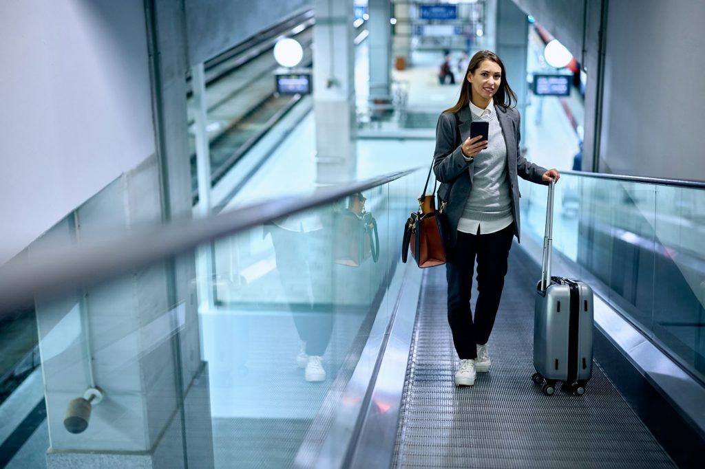 Young businesswoman with cell phone and suitcase at train station.